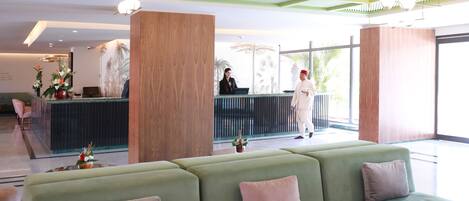Un área de recepción con un sofá verde, mostrador de madera y ventanas amplias.