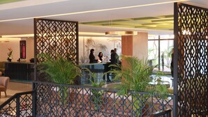 Un área de recepción con diseño moderno, que incluye un mostrador de recepción, un espacio de descanso y plantas decorativas.