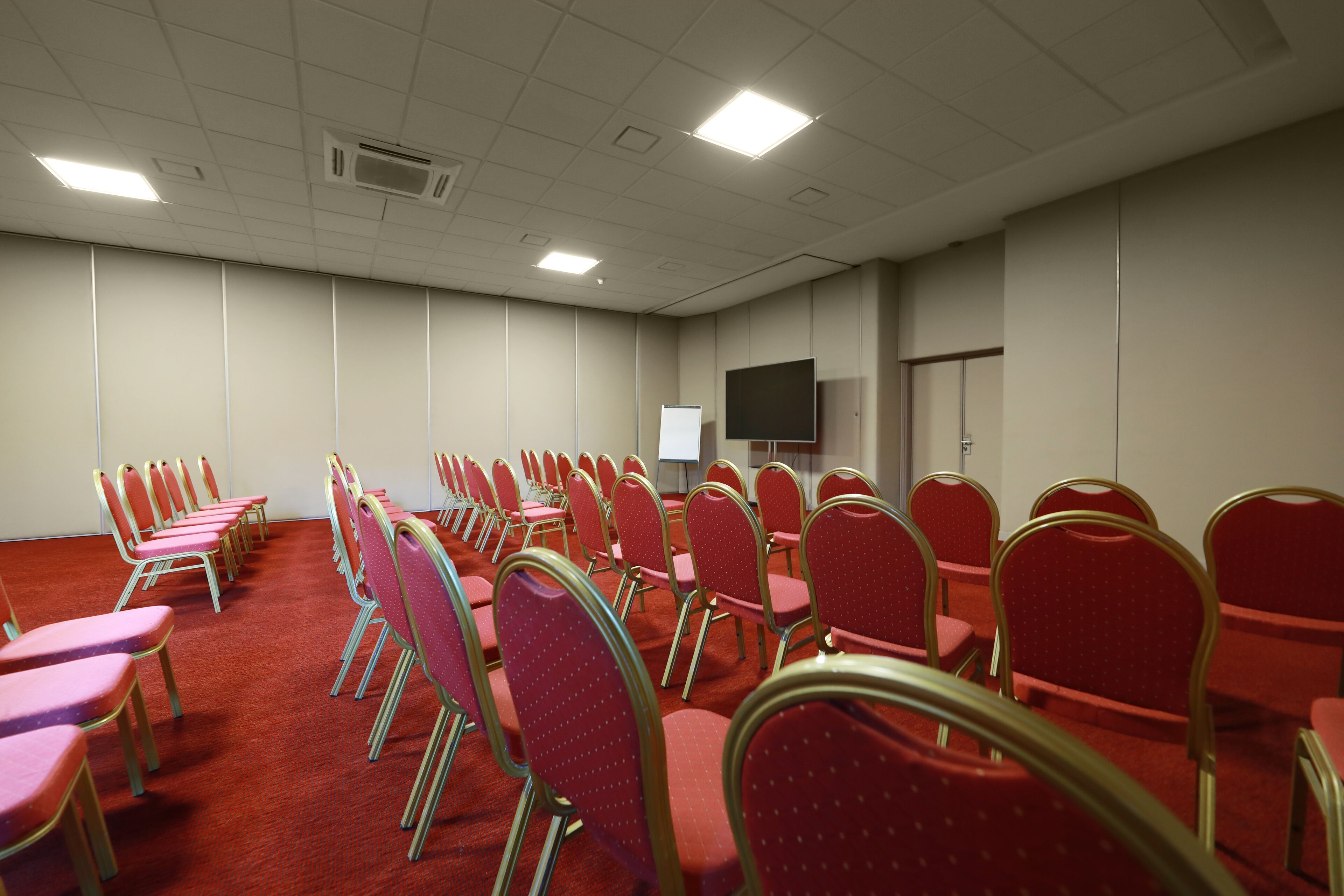 Una sala de conferencias con filas de sillas rojas y una pizarra.