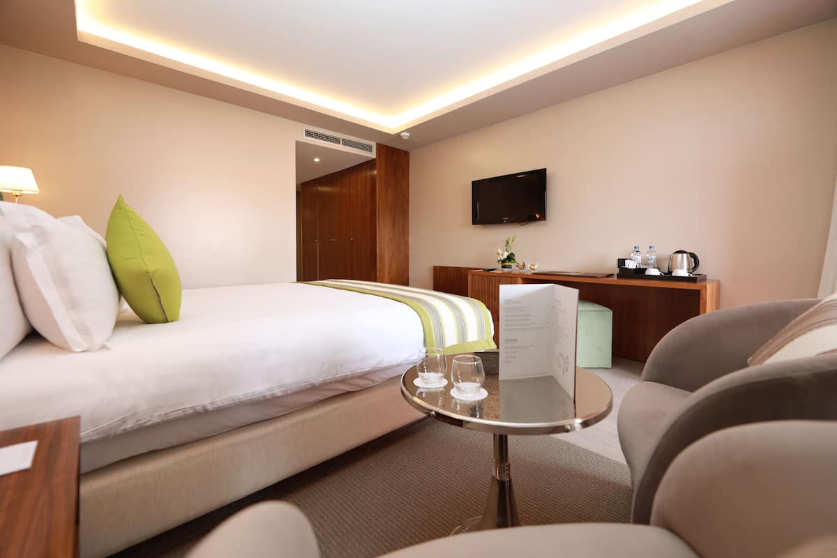 A hotel room with a bed, a desk, a TV, and a small table with glasses and a menu.