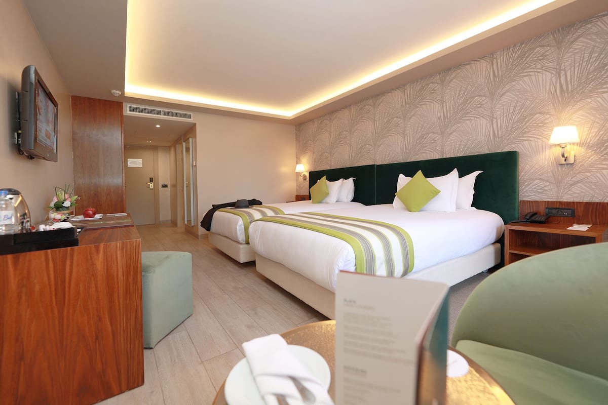 A hotel room with two beds, a desk, a chair, and a reception area.