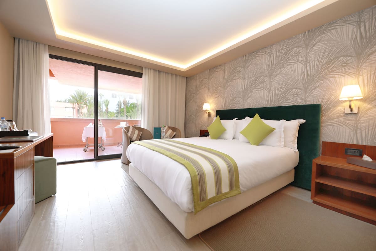 A hotel room with a large bed, a desk, a chair, and a view of the outside.