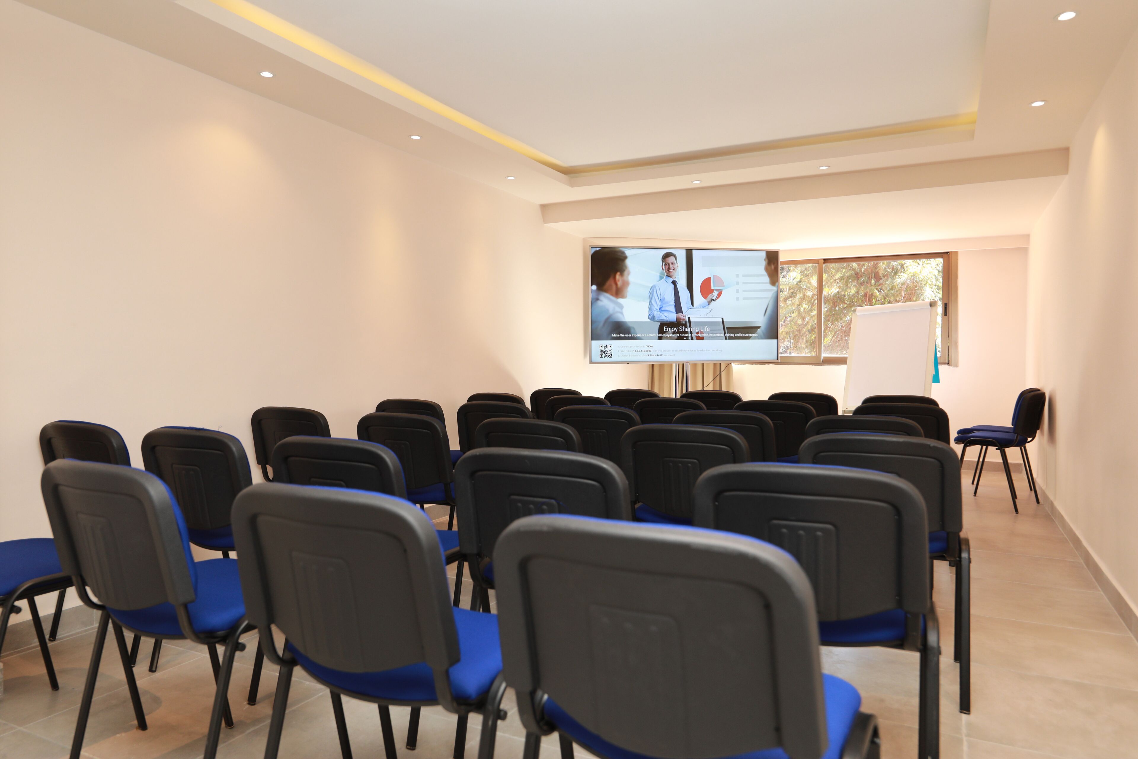 A conference room with rows of chairs, a projection screen, and a whiteboard.
