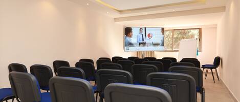 A conference room with rows of chairs, a projection screen, and a whiteboard.