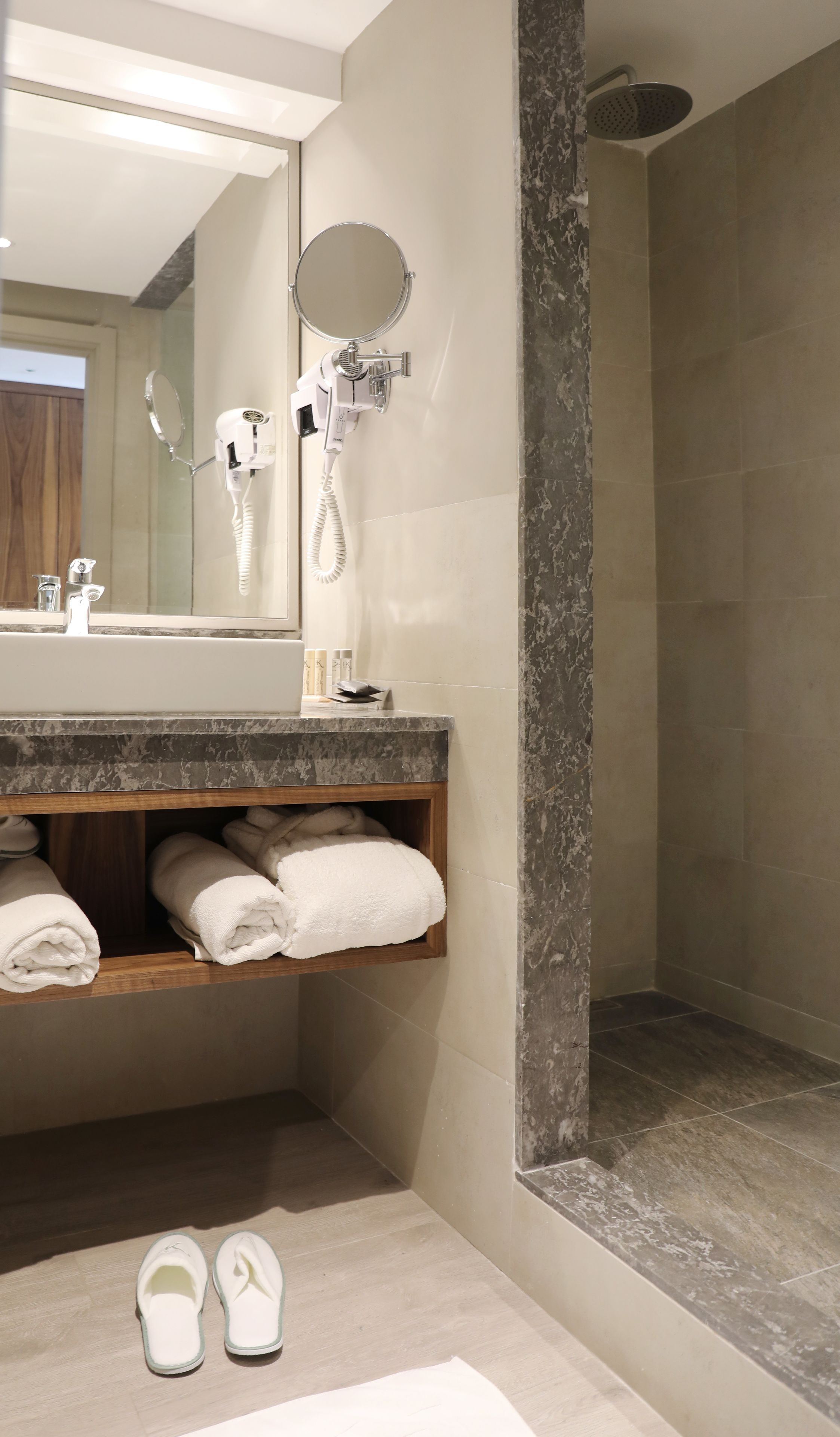 Een badkamer met een marmeren wastafelmeubel, een inloopdouche en een spiegel met een ronde lijst.