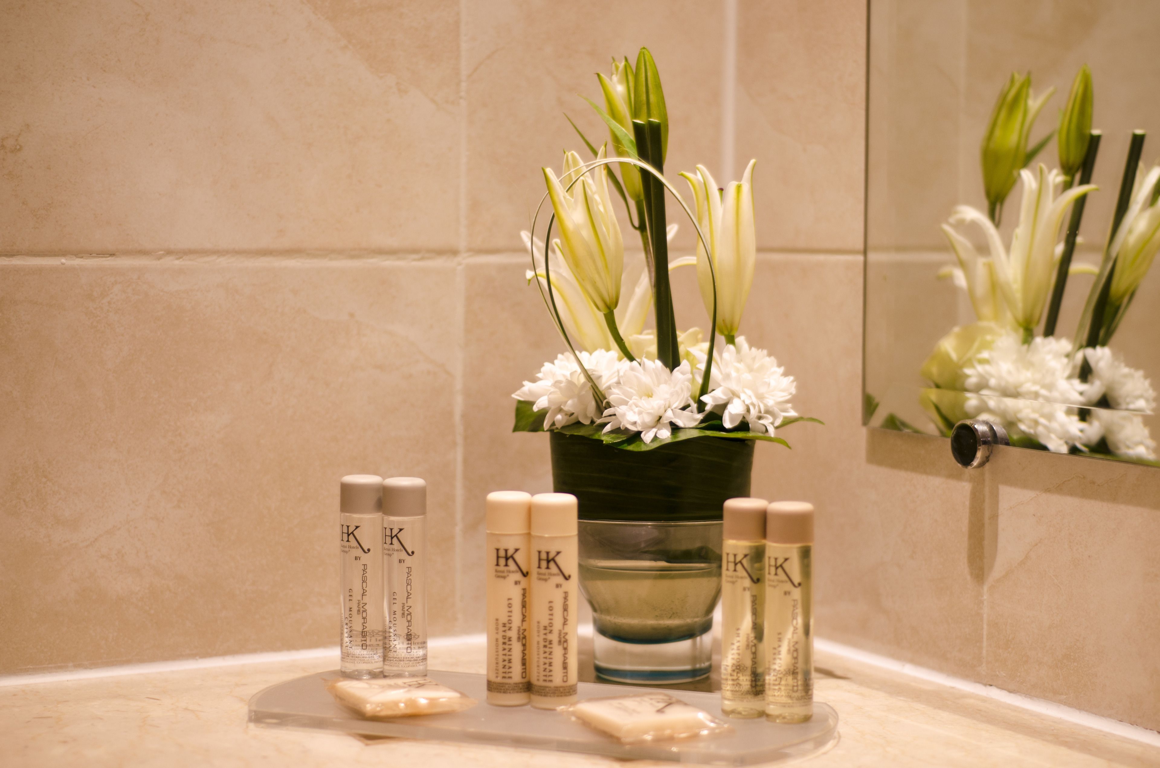 A bathroom vanity with toiletries, a vase of flowers, and a mirror.