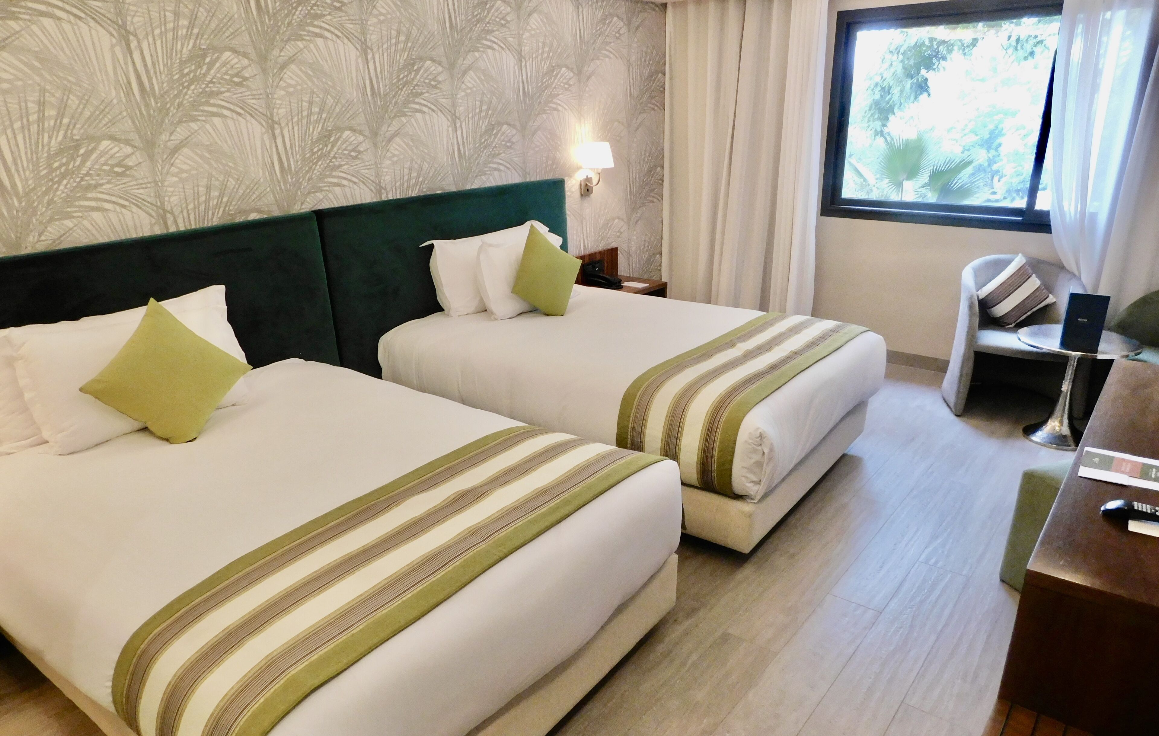 Habitación de hotel con dos camas, un escritorio, una silla, una computadora portátil y una ventana con vistas a árboles.