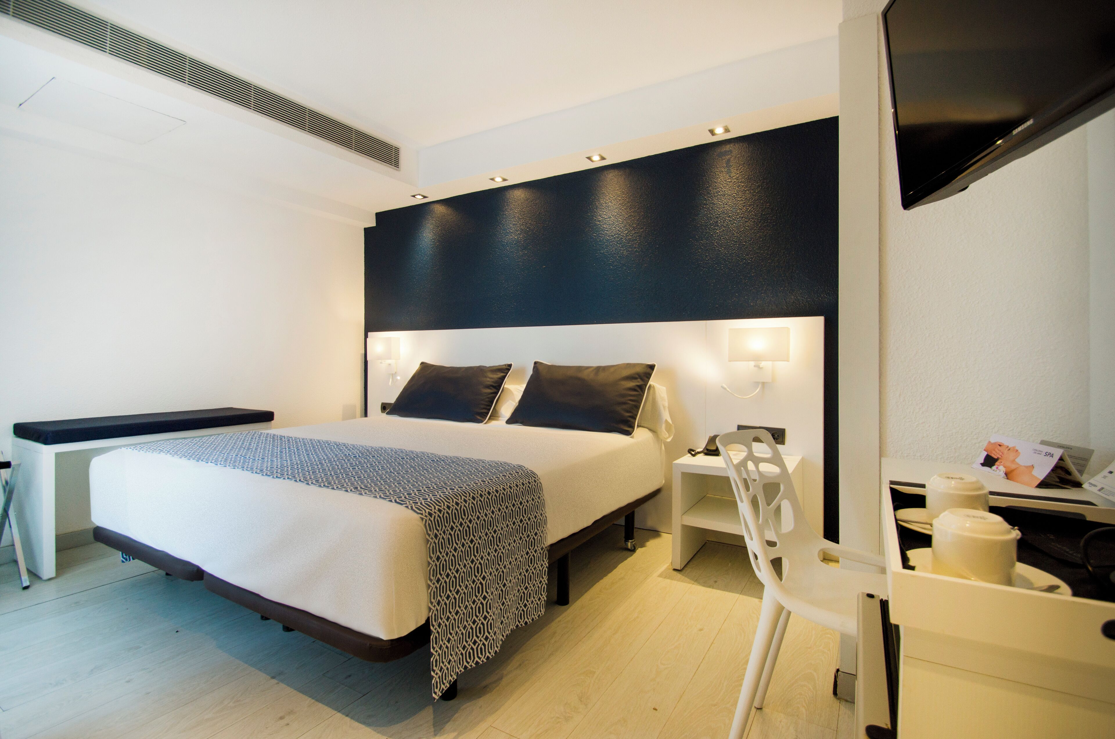 A modern hotel room with a large bed, bedside tables, a desk, and a flat-screen TV.
