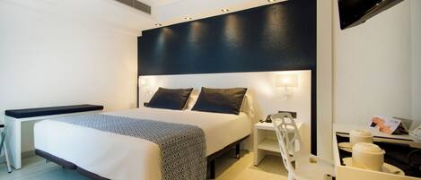 A modern hotel room with a large bed, bedside tables, a desk, and a flat-screen TV.