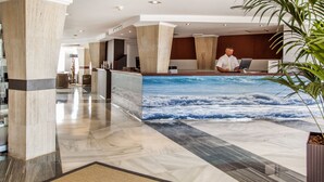 A hotel reception area with a large wall mural of ocean waves, marble flooring, and a reception desk. - Catalonia Del Mar - Adults Only (Son Servera)