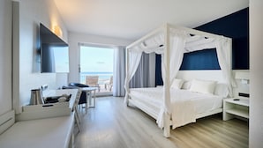 A modern hotel room with a four-poster bed, a desk with a chair, a flat-screen TV, and a balcony with a view. - Catalonia Del Mar - Adults Only (Son Servera)