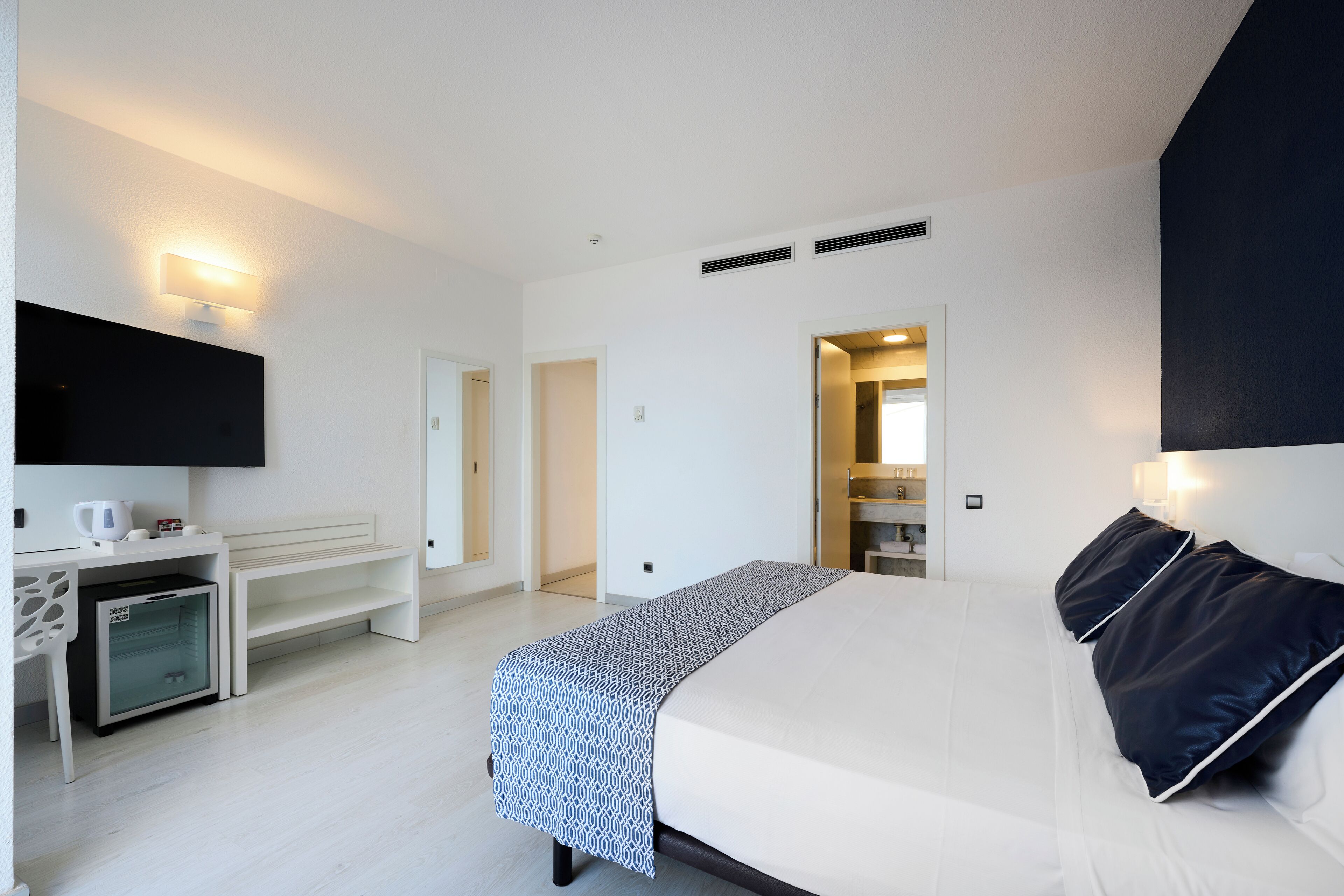 Una habitación de hotel moderna con una cama grande, un televisor de pantalla plana, un escritorio y un vestidor.