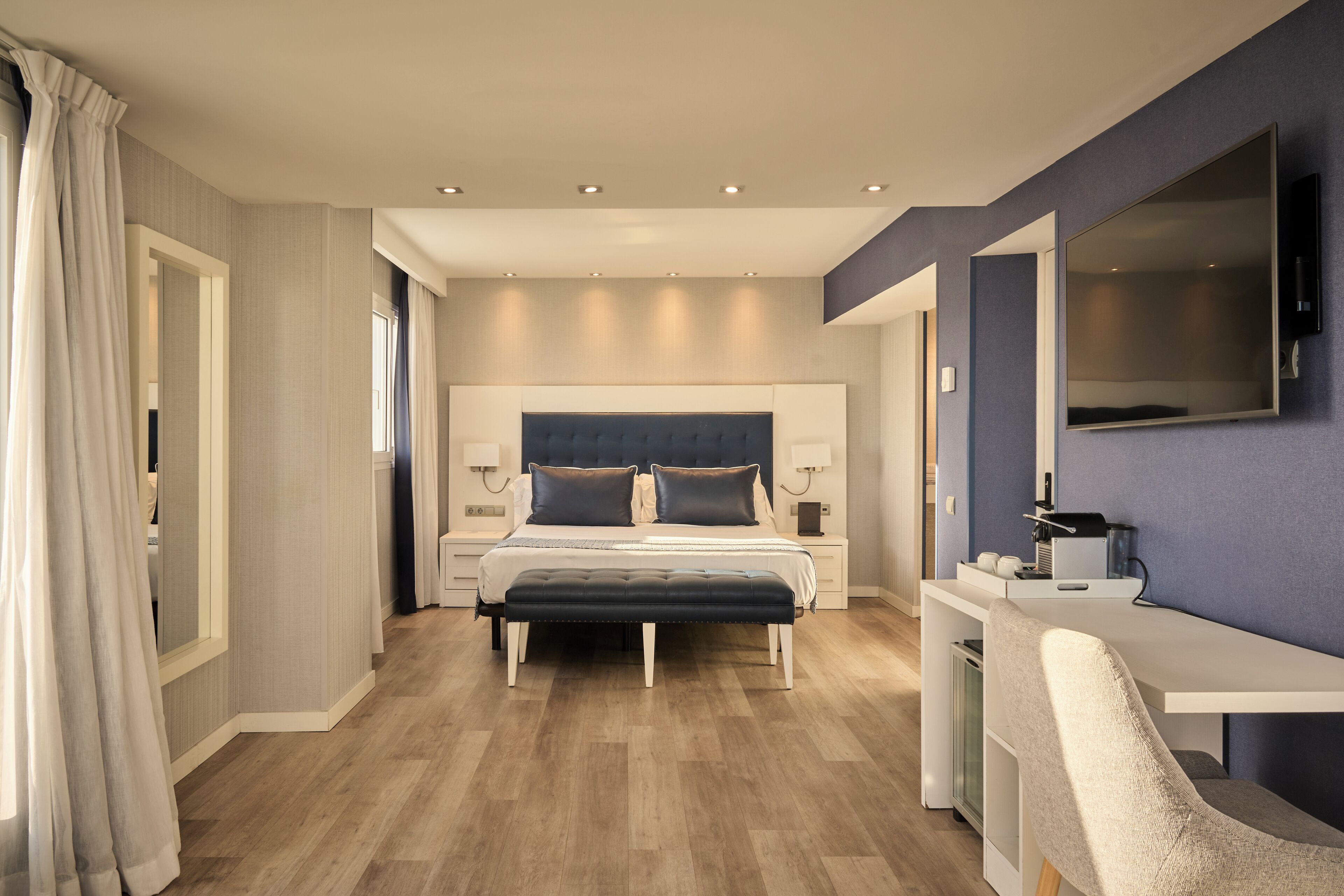 A modern bedroom with a large bed, bedside tables, a desk, and a mirror.