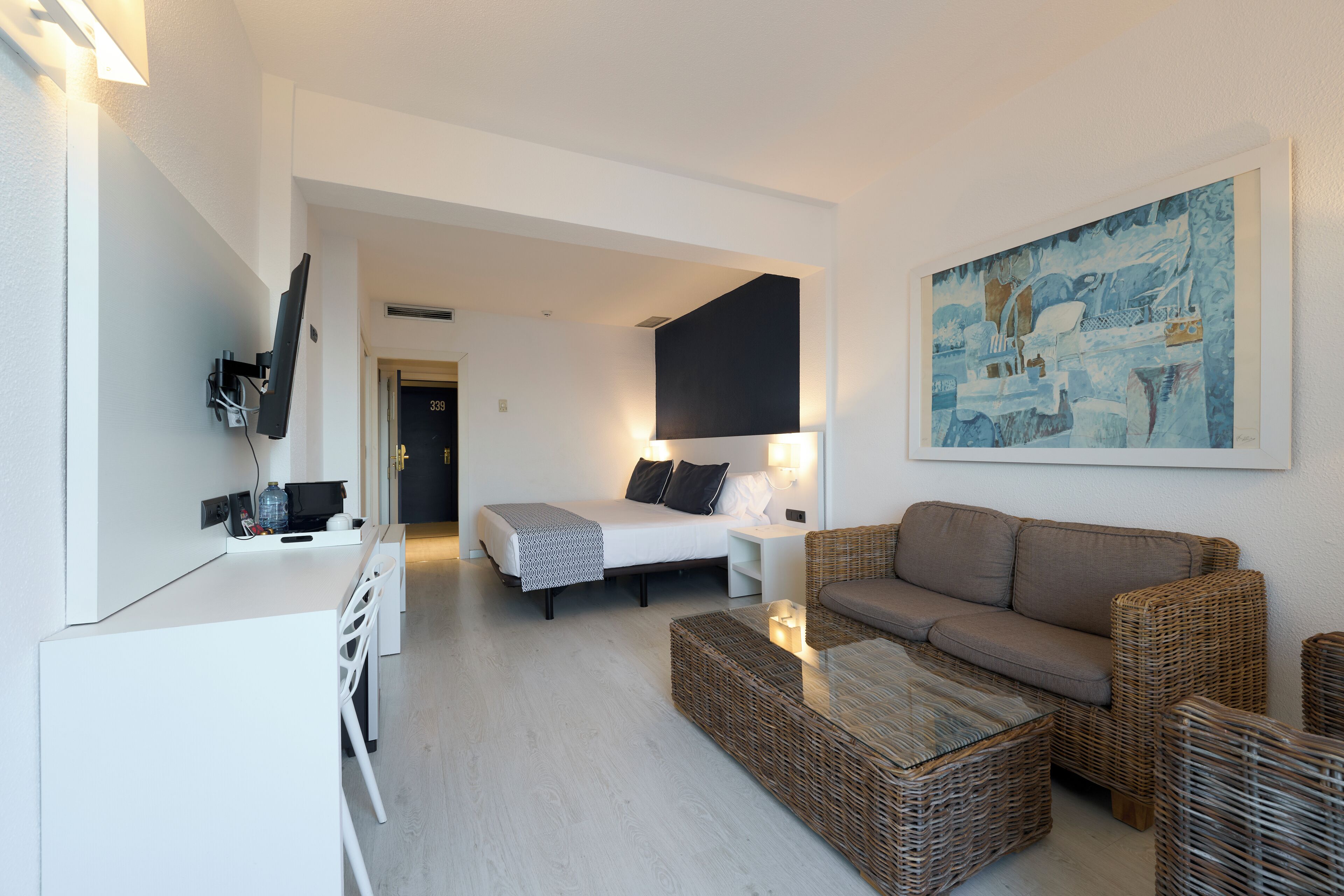 Una habitación de hotel moderna con cama, sofá, mesa de comedor y un cuadro en la pared.