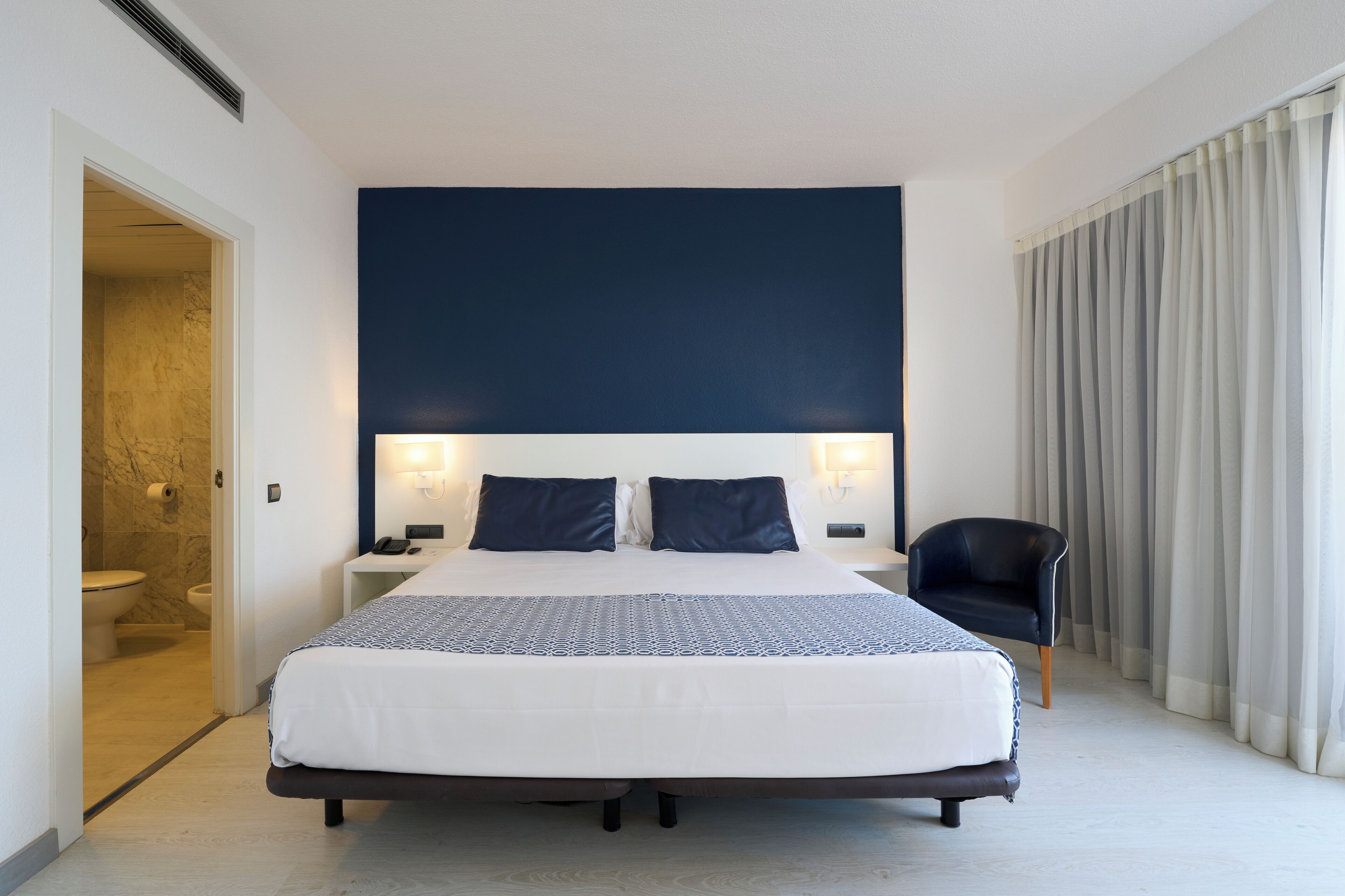 Een hotelkamer met een groot bed, een nachtkastje, een stoel en een badkamer die door een open deur zichtbaar is.