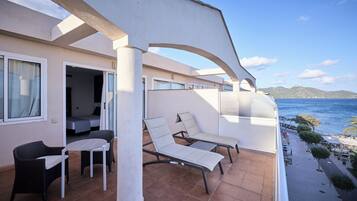 A balcony with two lounge chairs and a small table, overlooking a beach and the sea.