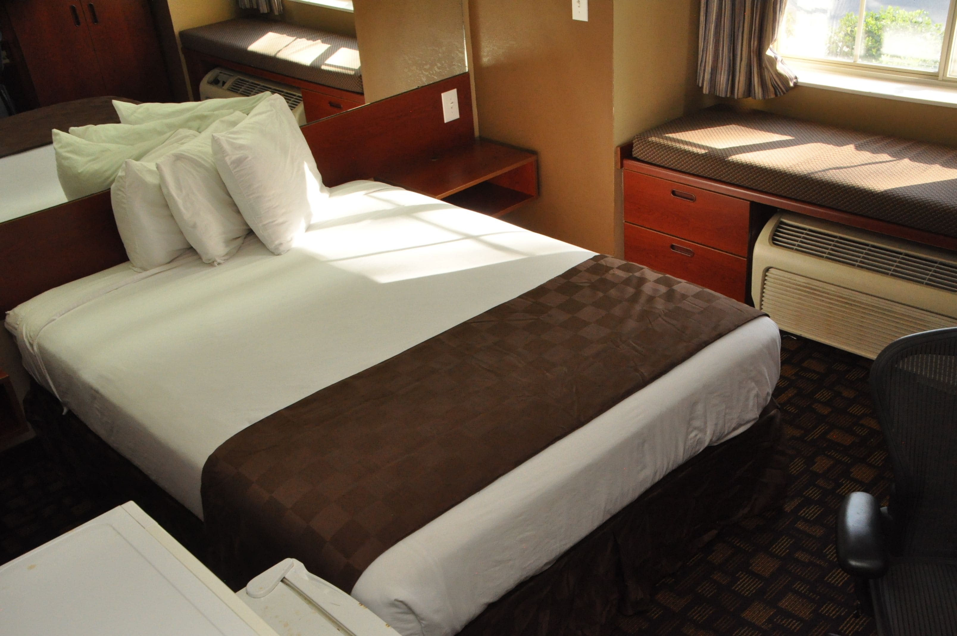 A hotel room with a bed, a desk, a chair, and a window.