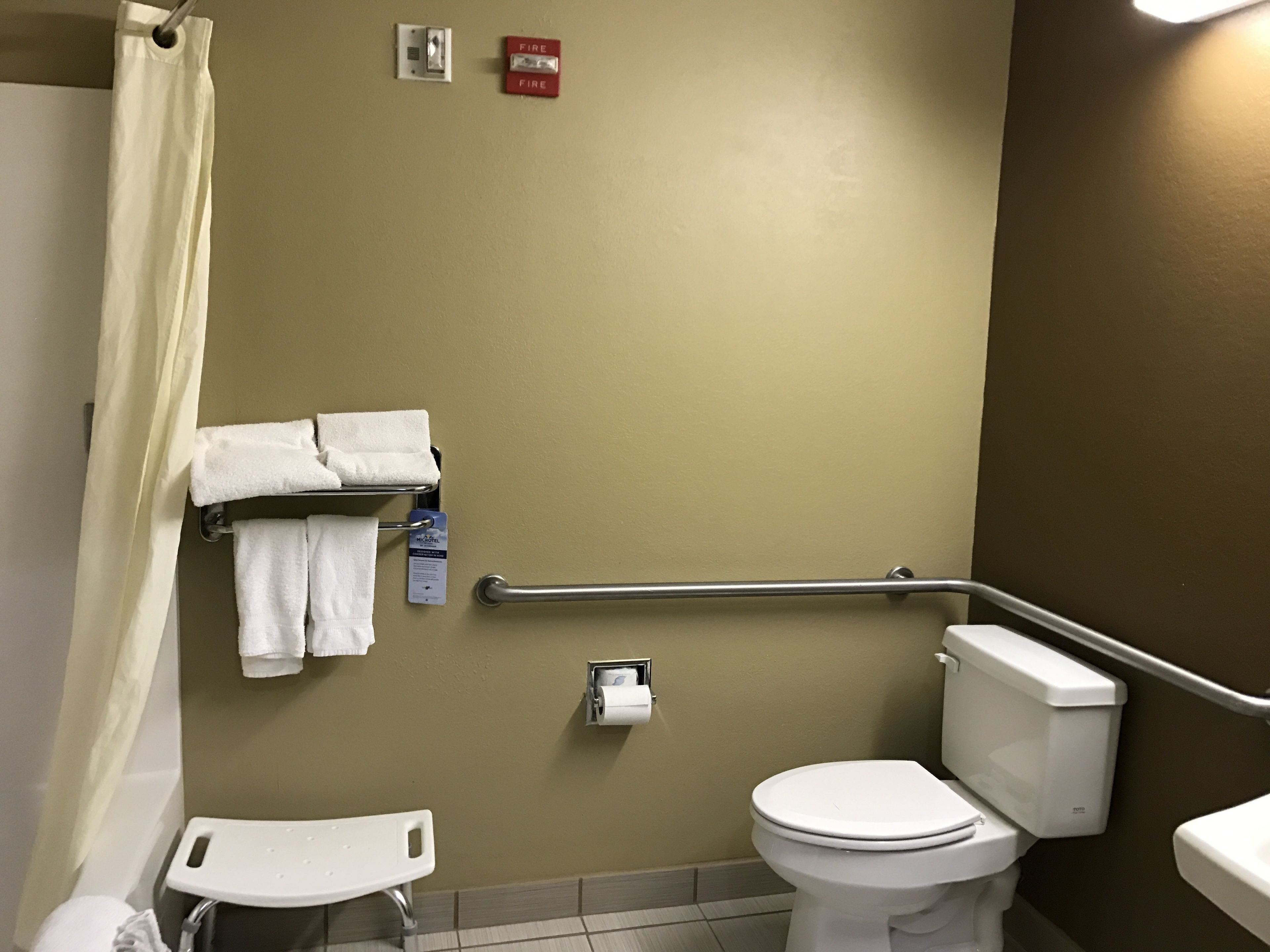 Un bagno con il water, un corrimano, un portaserviti e un rilevatore di fumo.