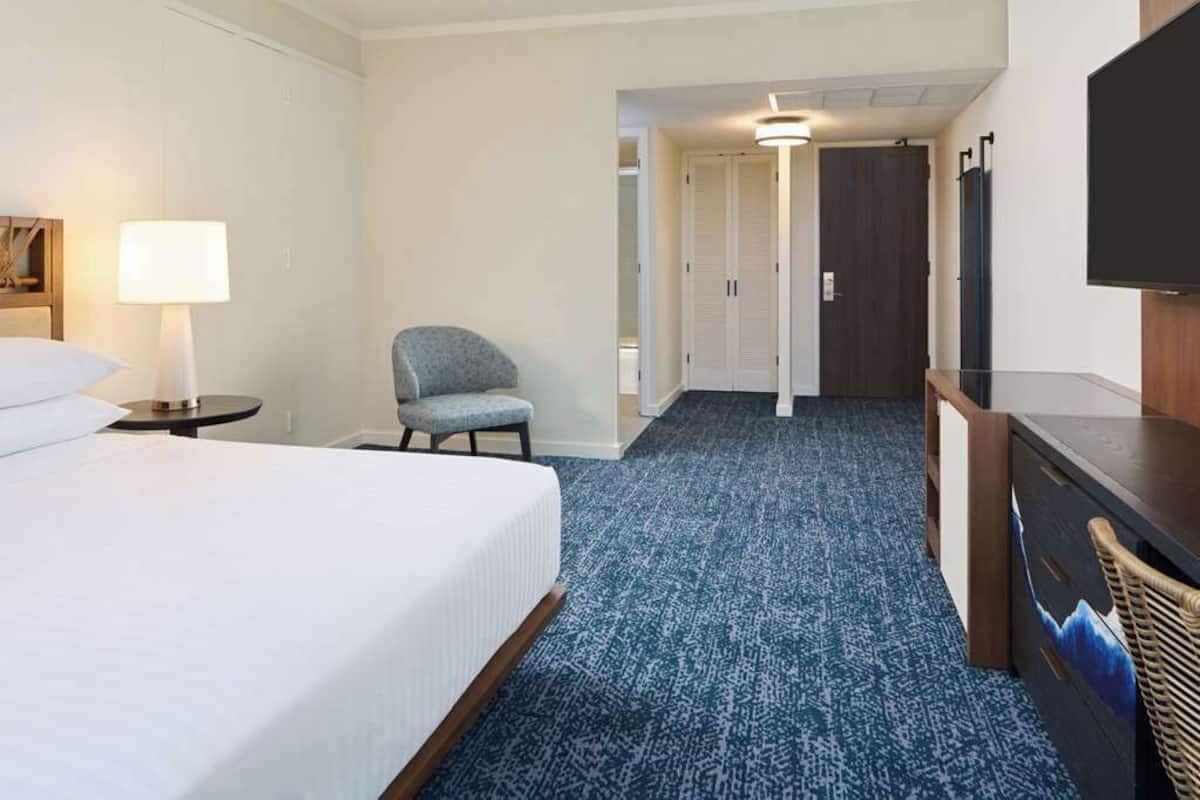 Une chambre d’hôtel comprenant un lit, une chaise, un bureau, une télévision et une armoire.