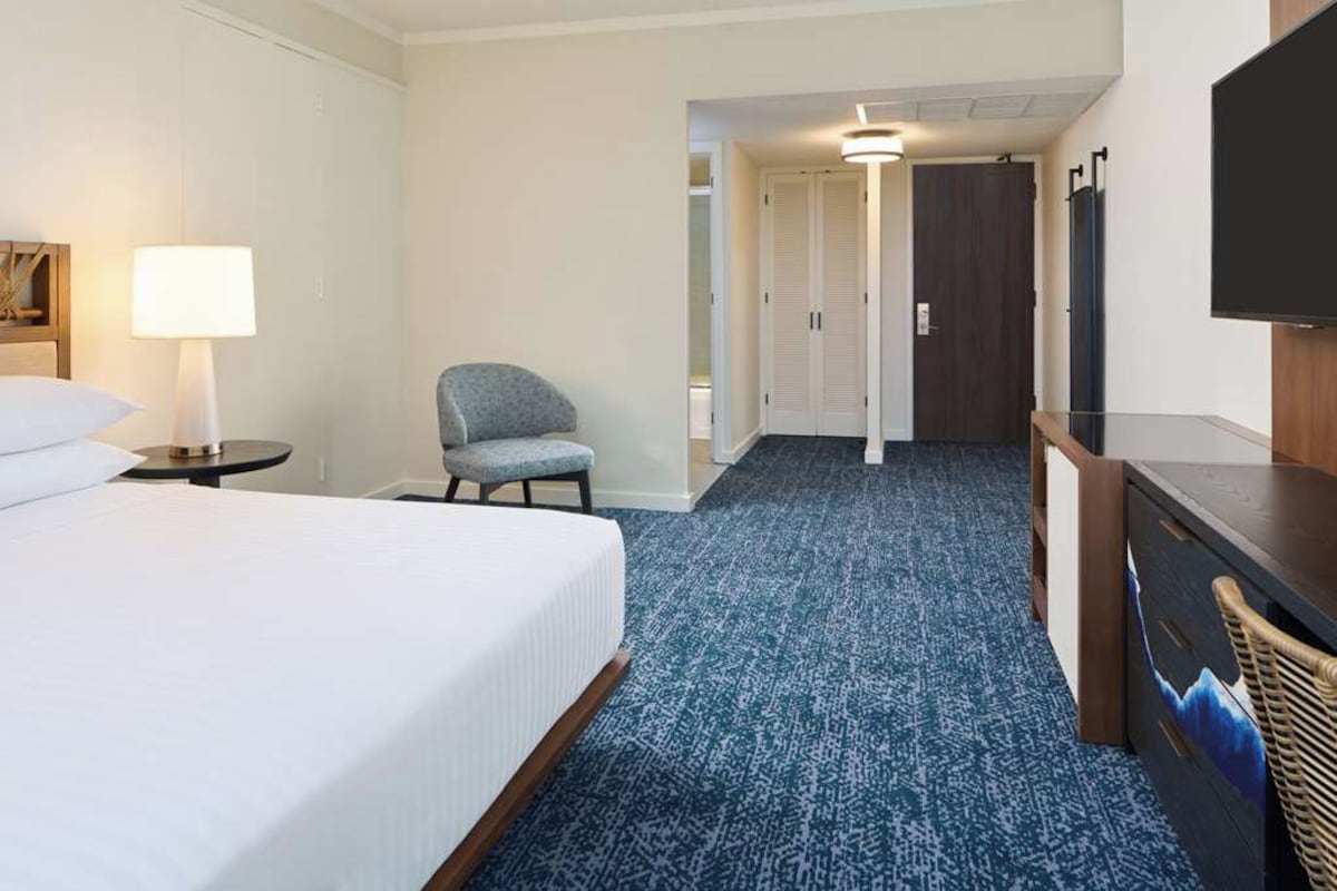 A hotel room with a bed, a chair, a desk, a TV, and a wardrobe.