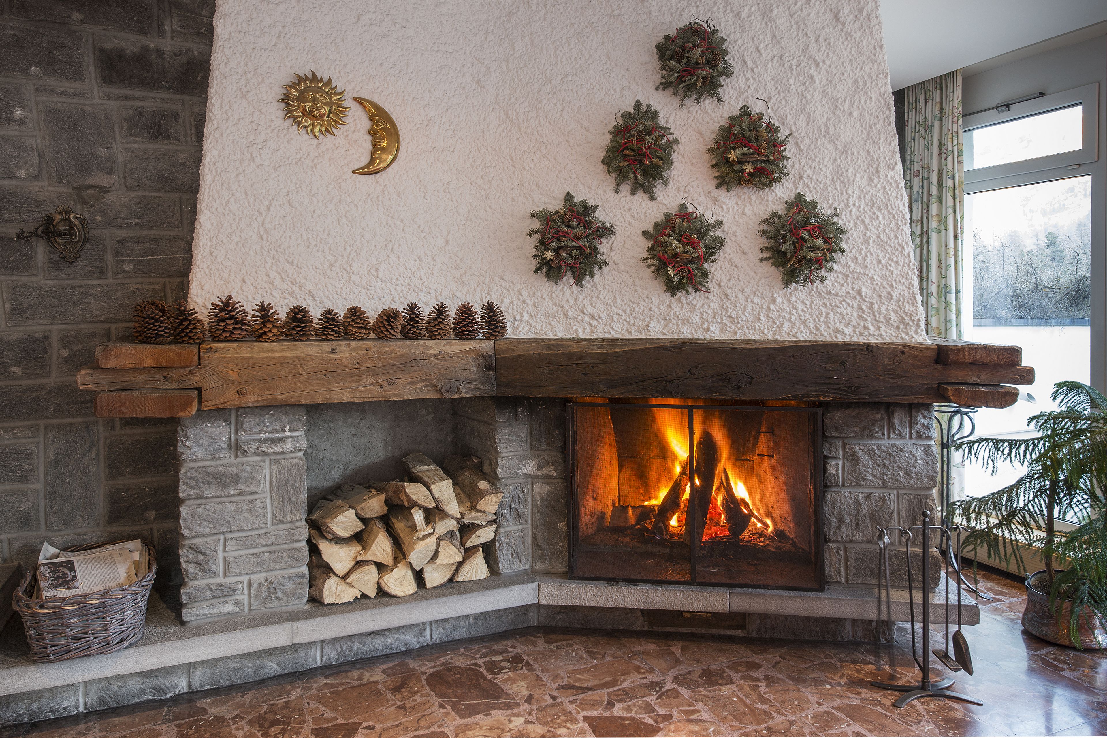 A stone fireplace with a fire, pine cones, and Christmas wreaths on the wall.