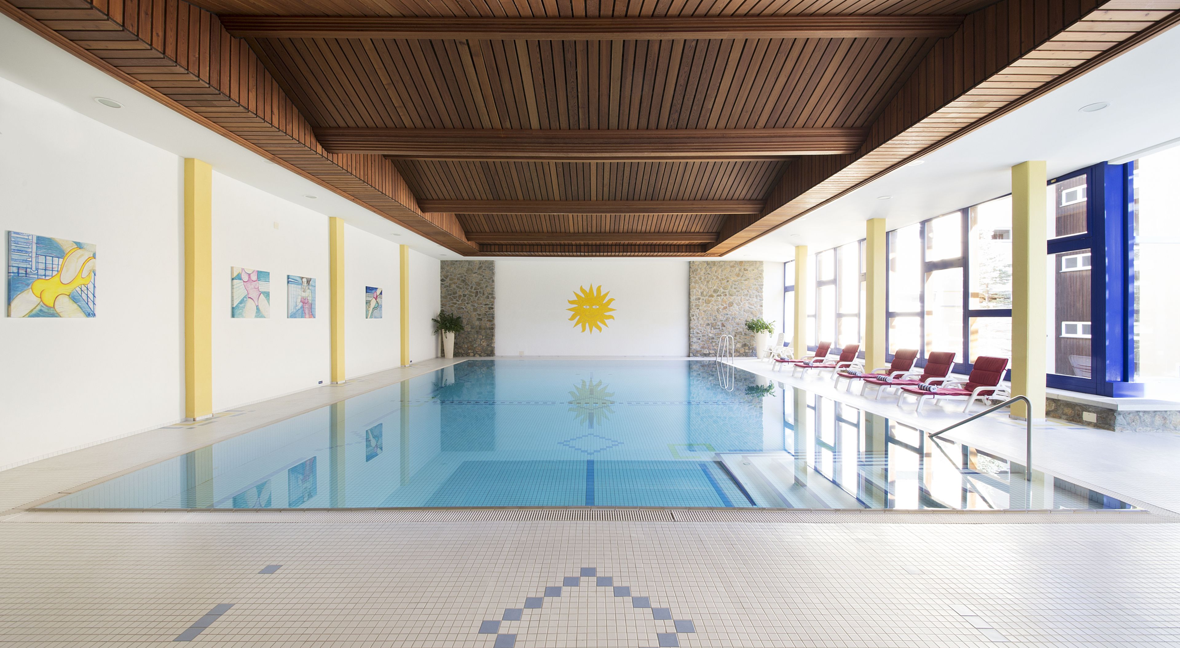 Una piscina interior con un mural de sol, sillones de descanso y obras de arte en las paredes.