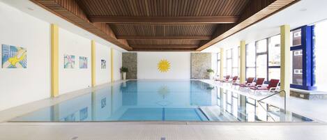 Una piscina interior con un mural de sol, sillones de descanso y obras de arte en las paredes.