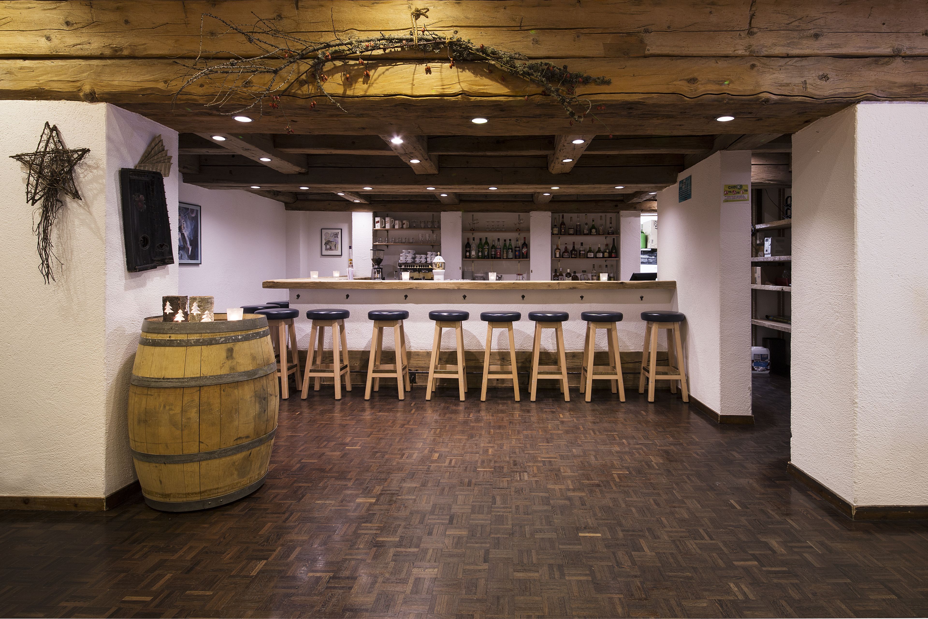 A bar area with wooden stools, a large barrel, and a wooden ceiling with exposed beams.