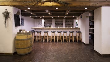 A bar area with wooden stools, a large barrel, and a wooden ceiling with exposed beams.