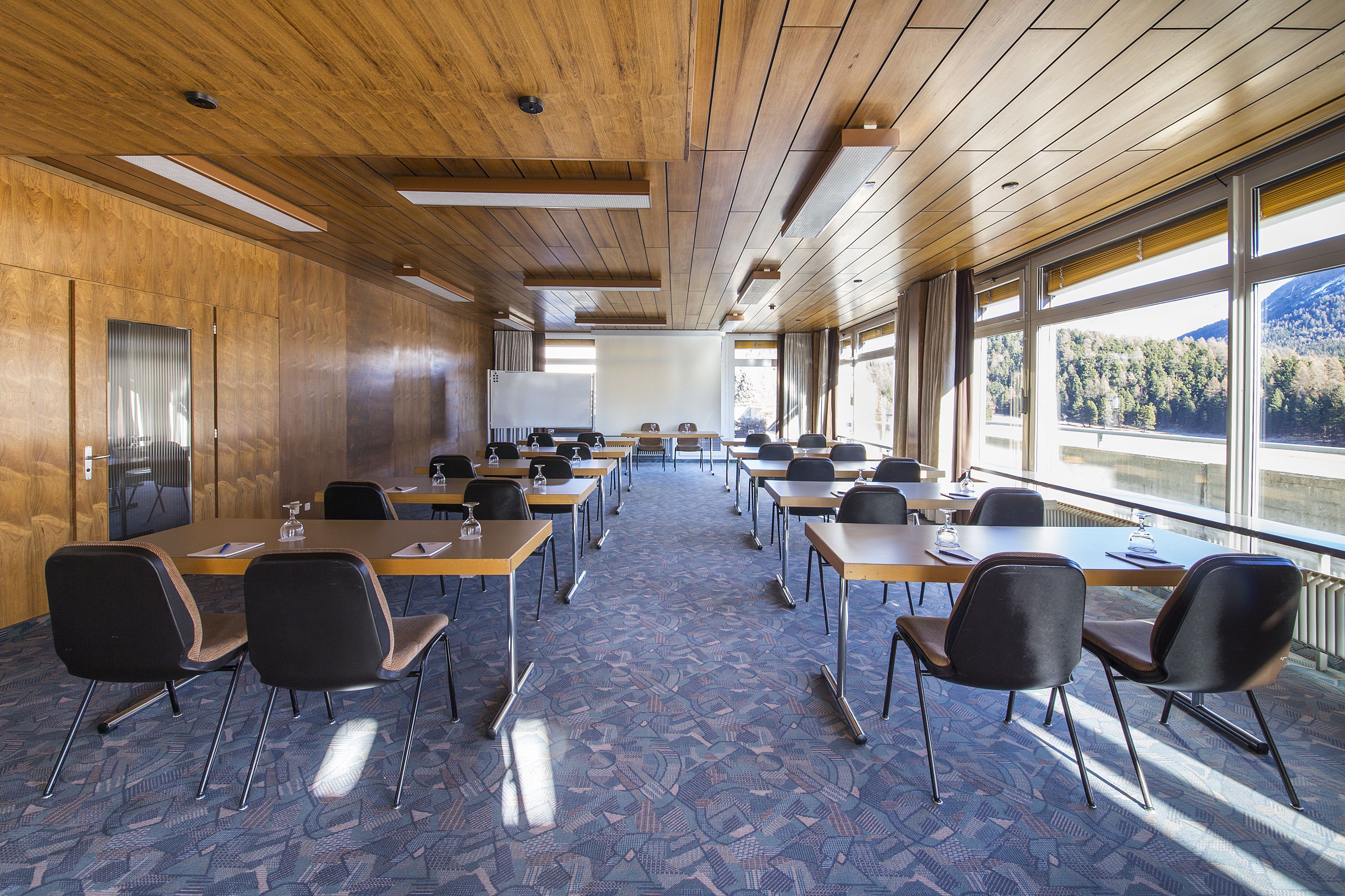Une salle de conférence aux murs lambrés, dotée de grandes fenêtres offrant une vue sur les montagnes et recouverte d’un tapis à motifs.
