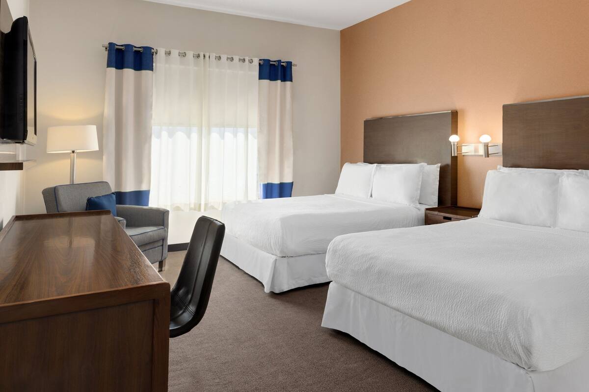 Une chambre d’hôtel avec deux lits, un bureau, une chaise, une télévision et une fenêtre avec des rideaux.