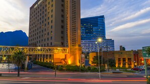 A hotel with a prominent sign, a modern building across the street, and a bridge overhead.