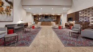 A spacious lobby with a central seating area, a reception desk, and a large artwork on the left.