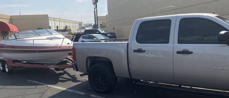 A pickup truck parked in a lot with a trailer attached, a boat on the trailer, and a building in the background.