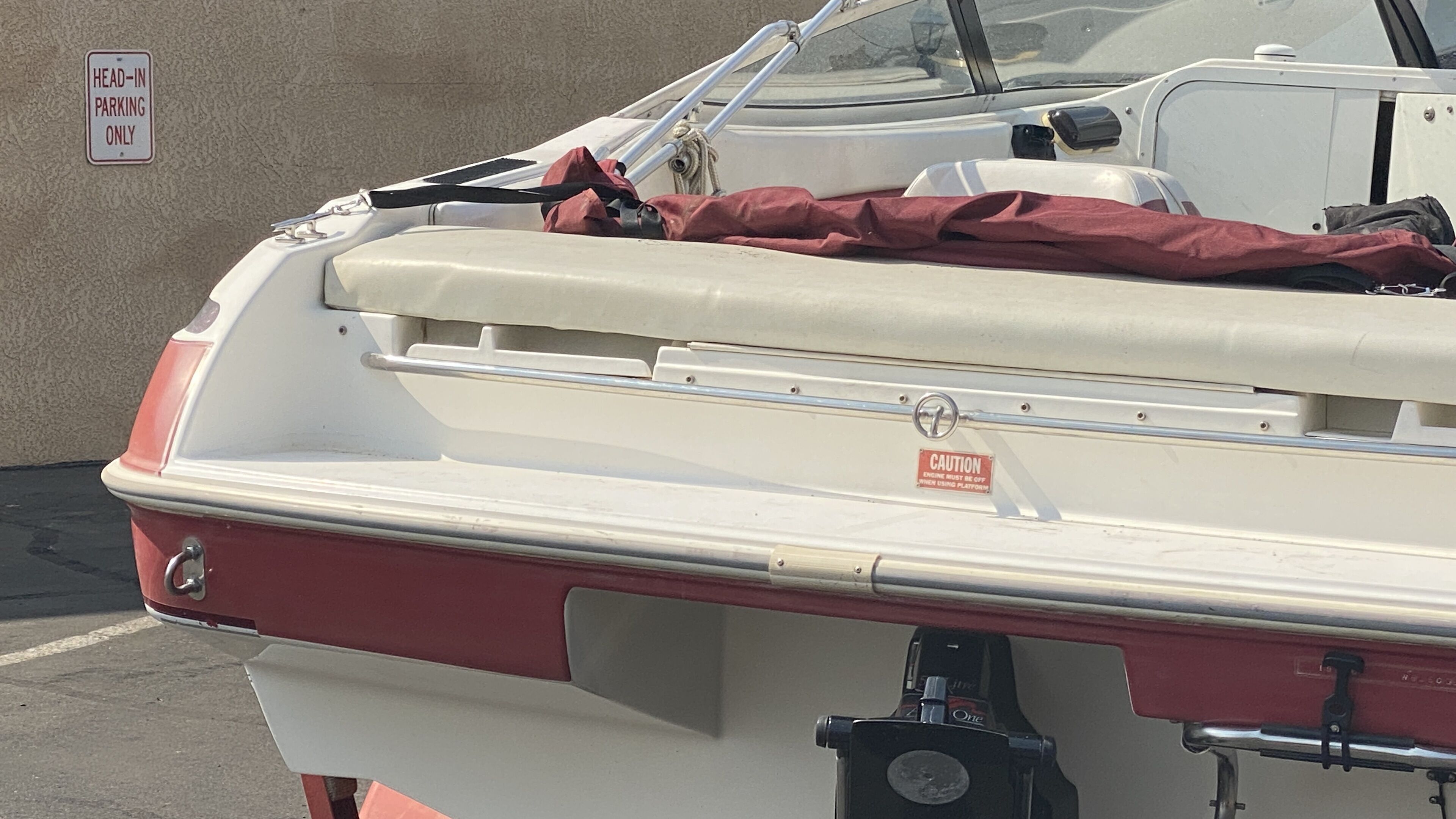 A boat with a head-in parking sign, a caution sign about engine use, and a red cover on the back.