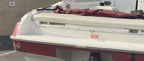 A boat with a head-in parking sign, a caution sign about engine use, and a red cover on the back.