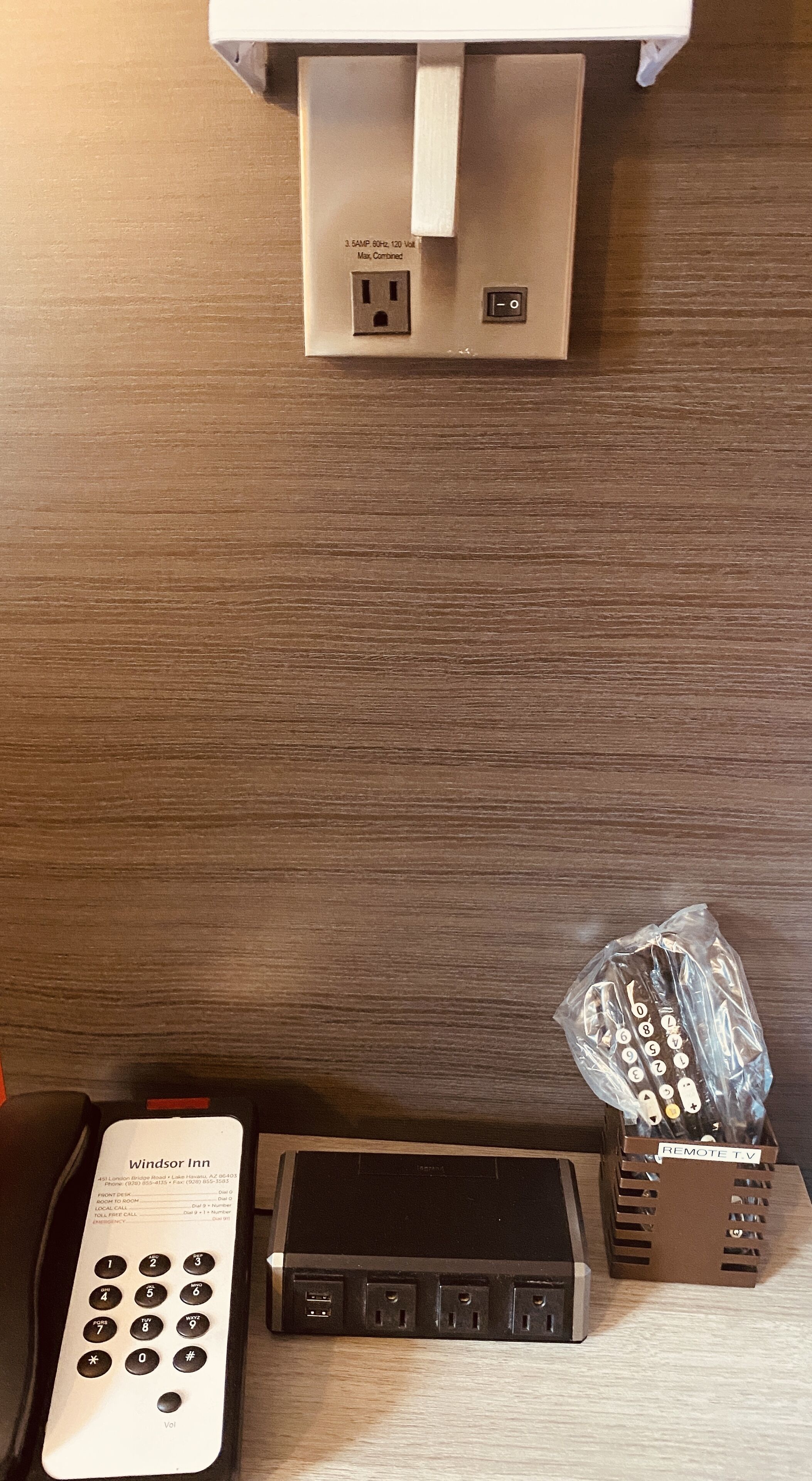 A hotel room with a remote control, a power strip, and a wall socket.
