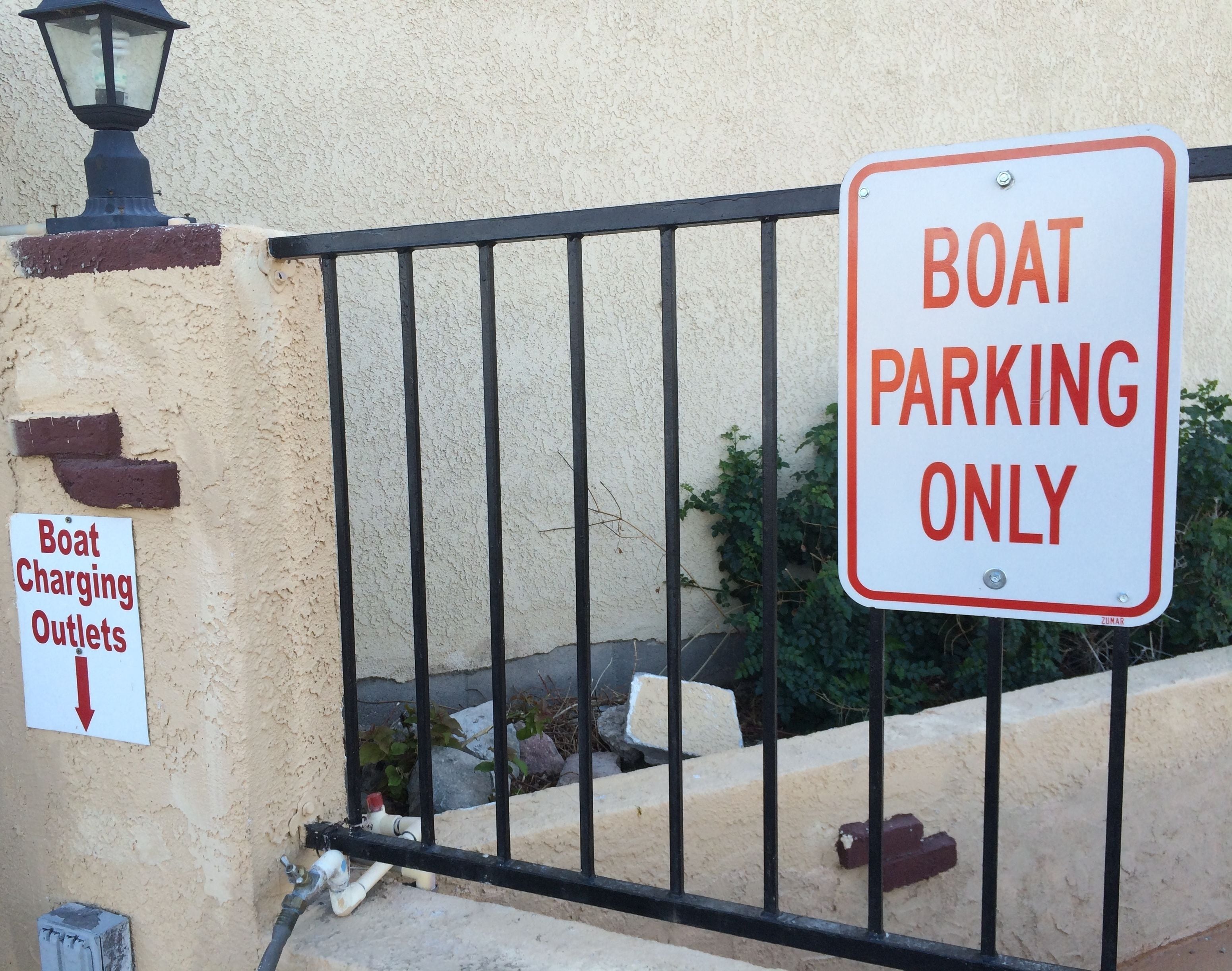 A boat charging outlet sign and a 'Boat Parking Only' sign on a fence.
