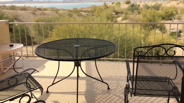 A balcony with a round table and two chairs, overlooking a scenic view of a lake and mountains.