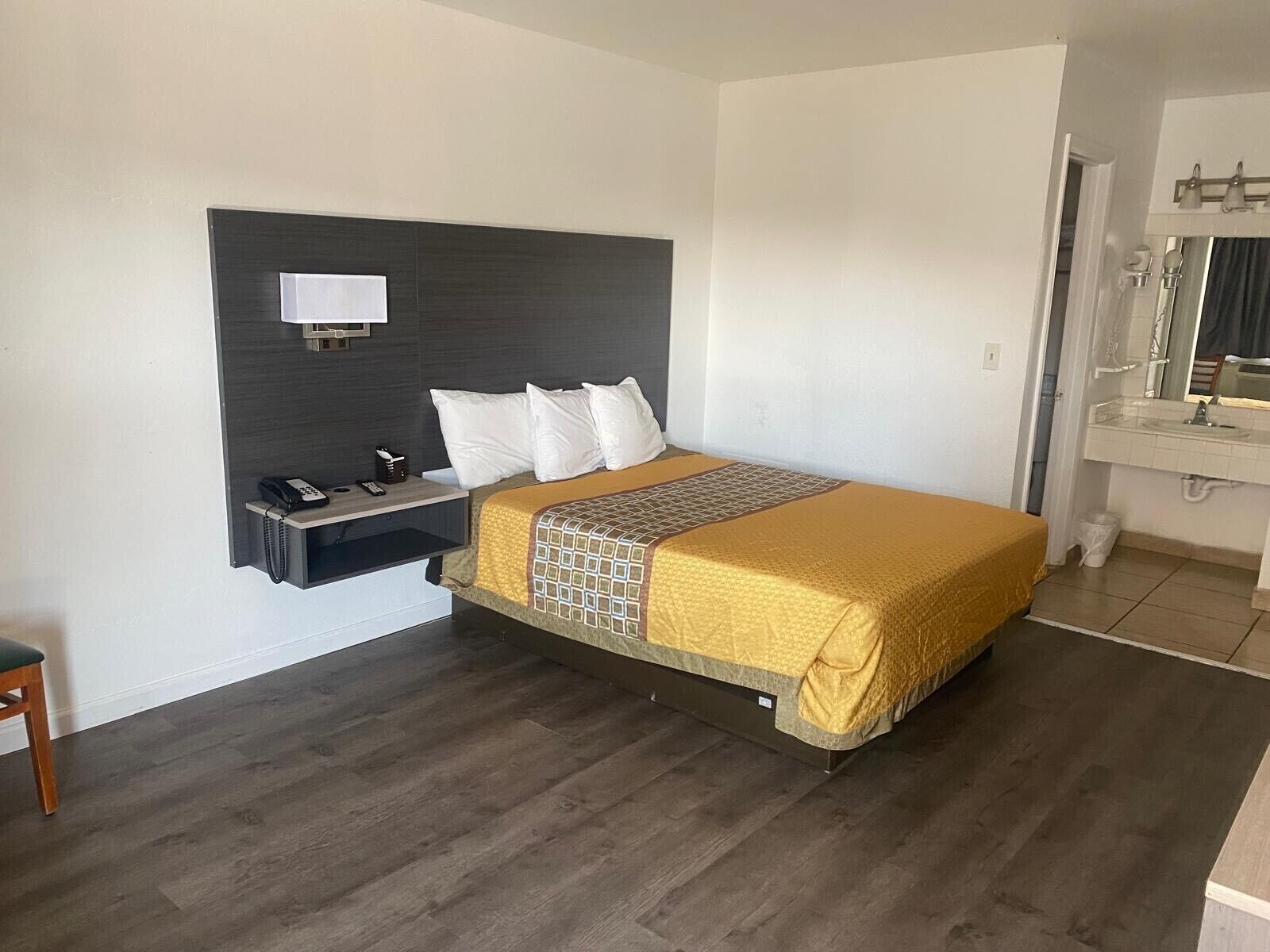 A hotel room with a bed, bedside table, phone, and a bathroom with a mirror and sink.