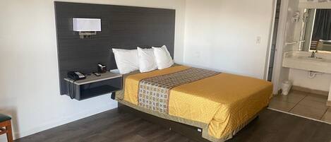 Une chambre d’hôtel comprenant un lit, une table de chevet, un téléphone et une salle de bain avec un miroir et un lavabo.
