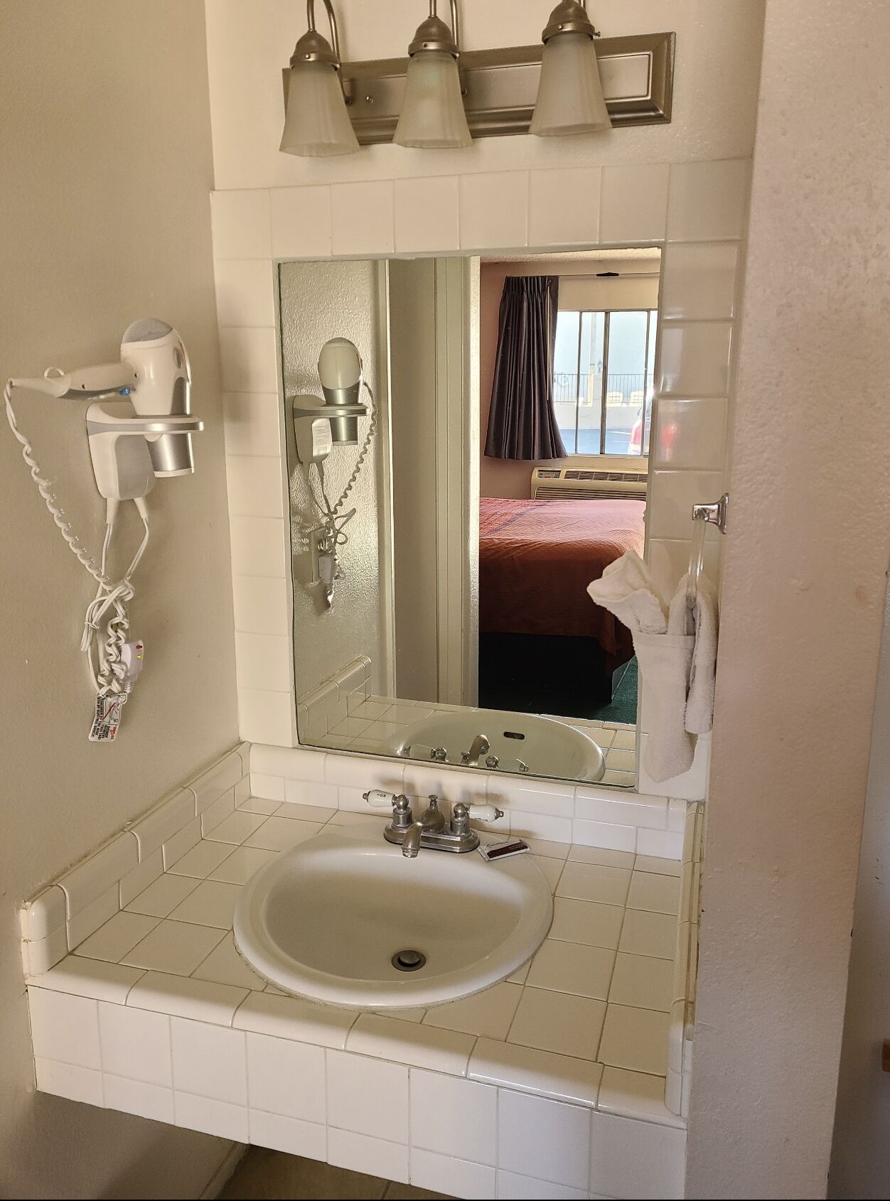 A bathroom with a sink, mirror, hairdryer, and towel rack.