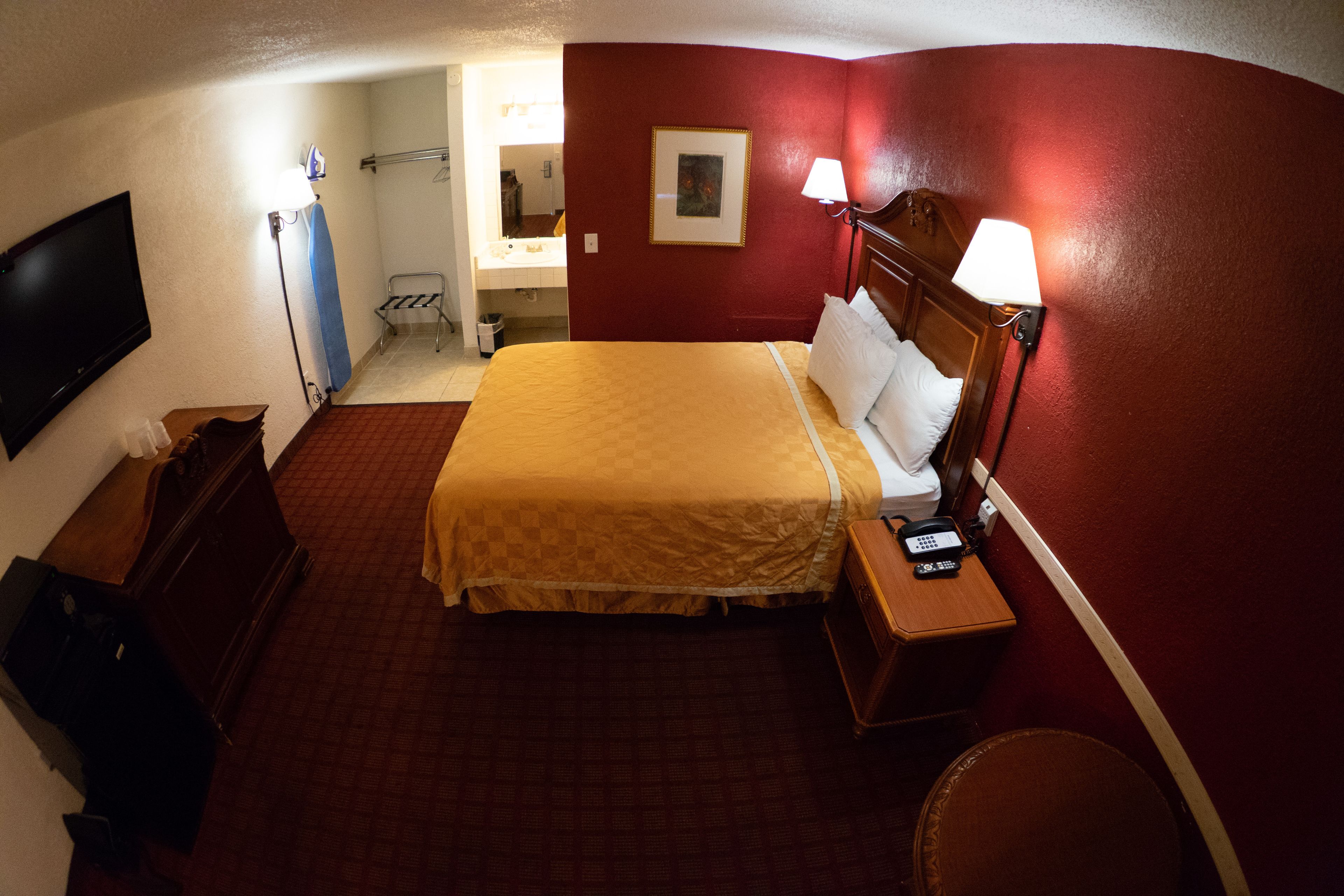 Una camera d'albergo con un letto, un comodino, una lampada e un televisore appeso al muro.