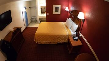 A hotel room with a bed, bedside table, lamp, and a television on the wall.