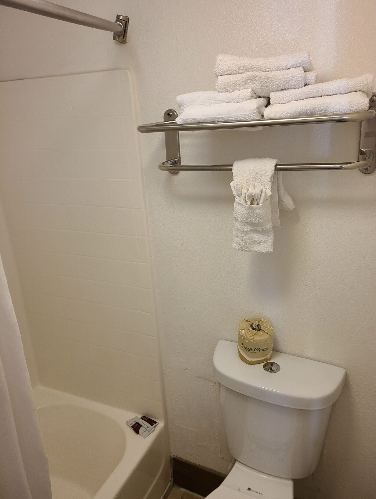 Un baño con bañera, inodoro, toallero con toallas dobladas y dispensador de papel higiénico.