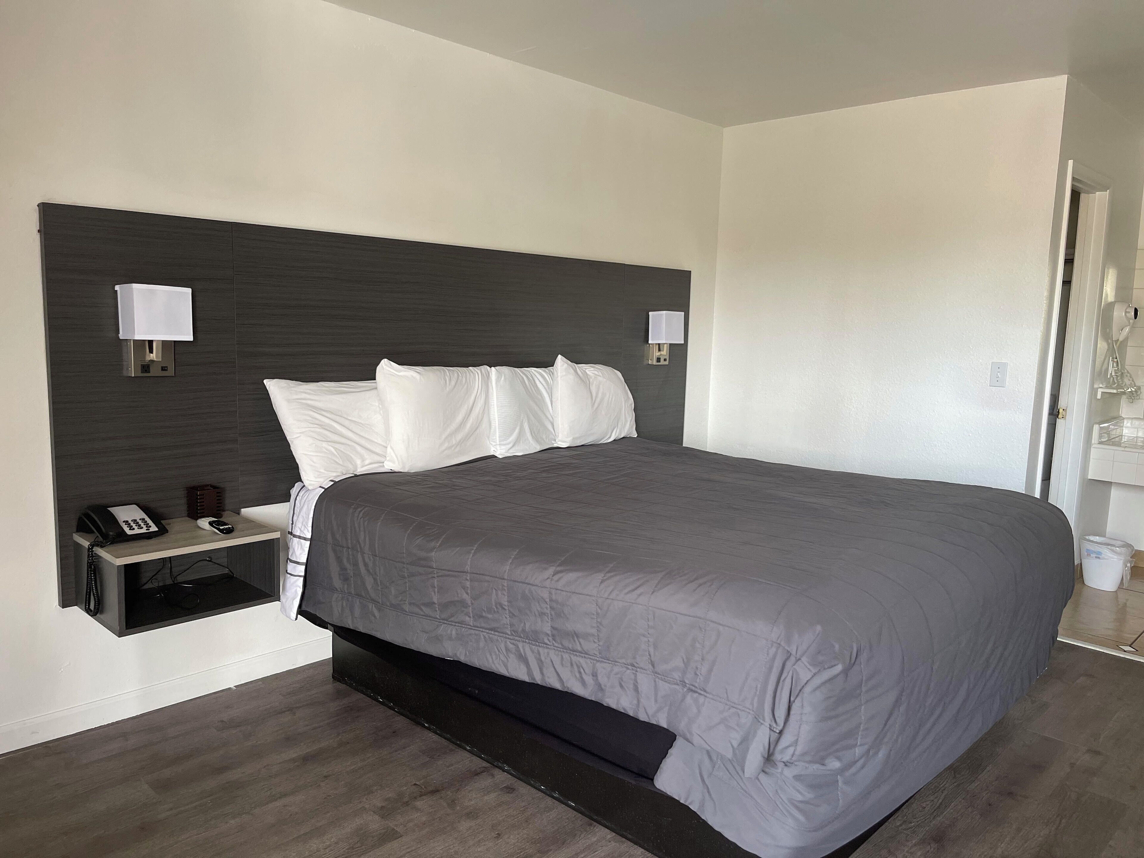 Una habitación de hotel moderna con una cama grande, una mesita de noche con teléfono y lámpara.