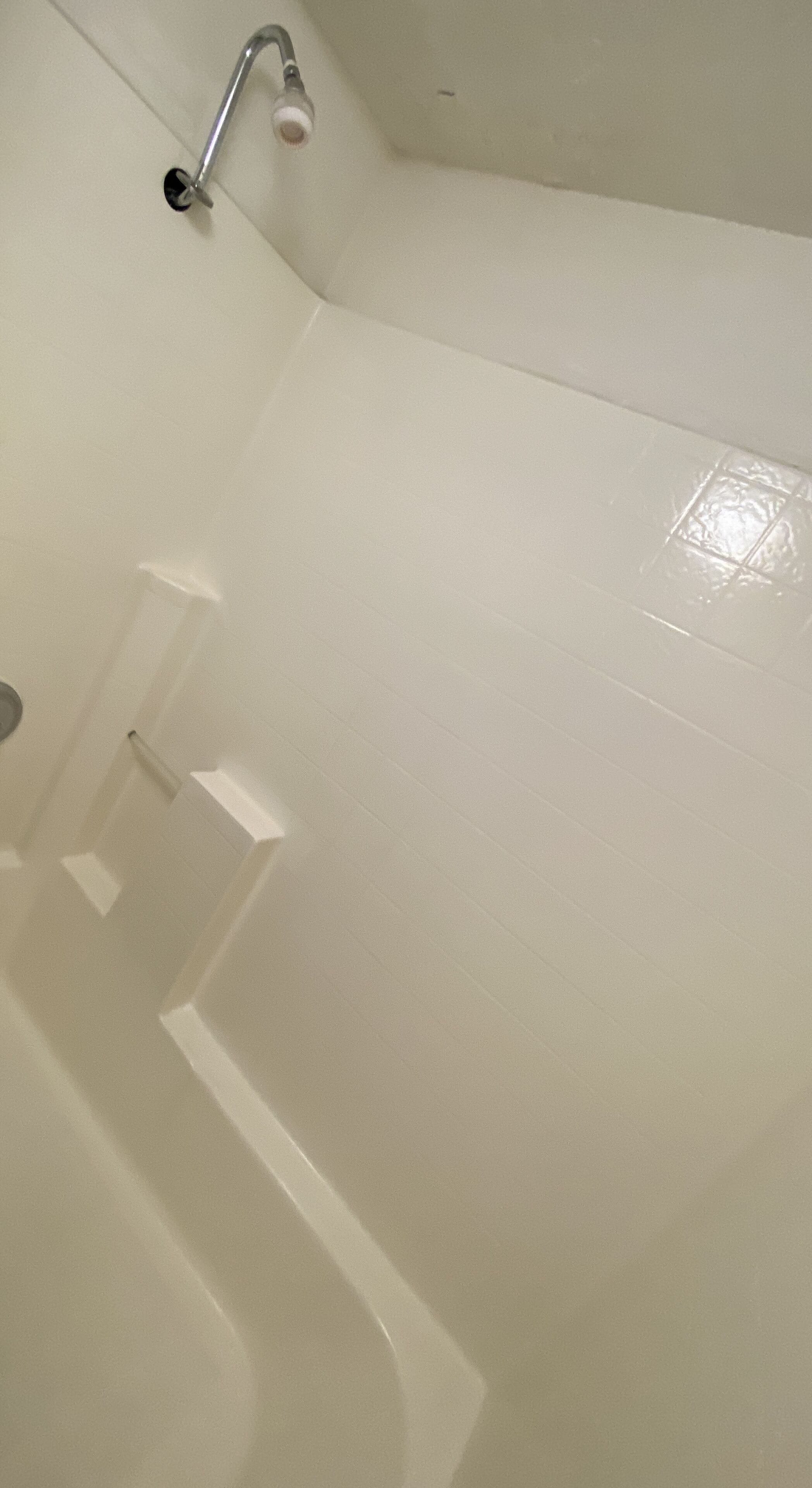 Une salle de bain avec des carreaux blancs, un espace douche et une barre d’appui.
