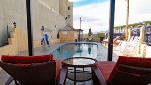 A pool area with lounge chairs, a small pool, and a view of mountains.