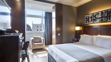 Een hotelkamer met een groot bed, een bureau, een stoel en een raam met uitzicht op gebouwen.