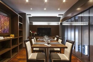 A modern dining area with a long table, chairs, and a television screen in the background.